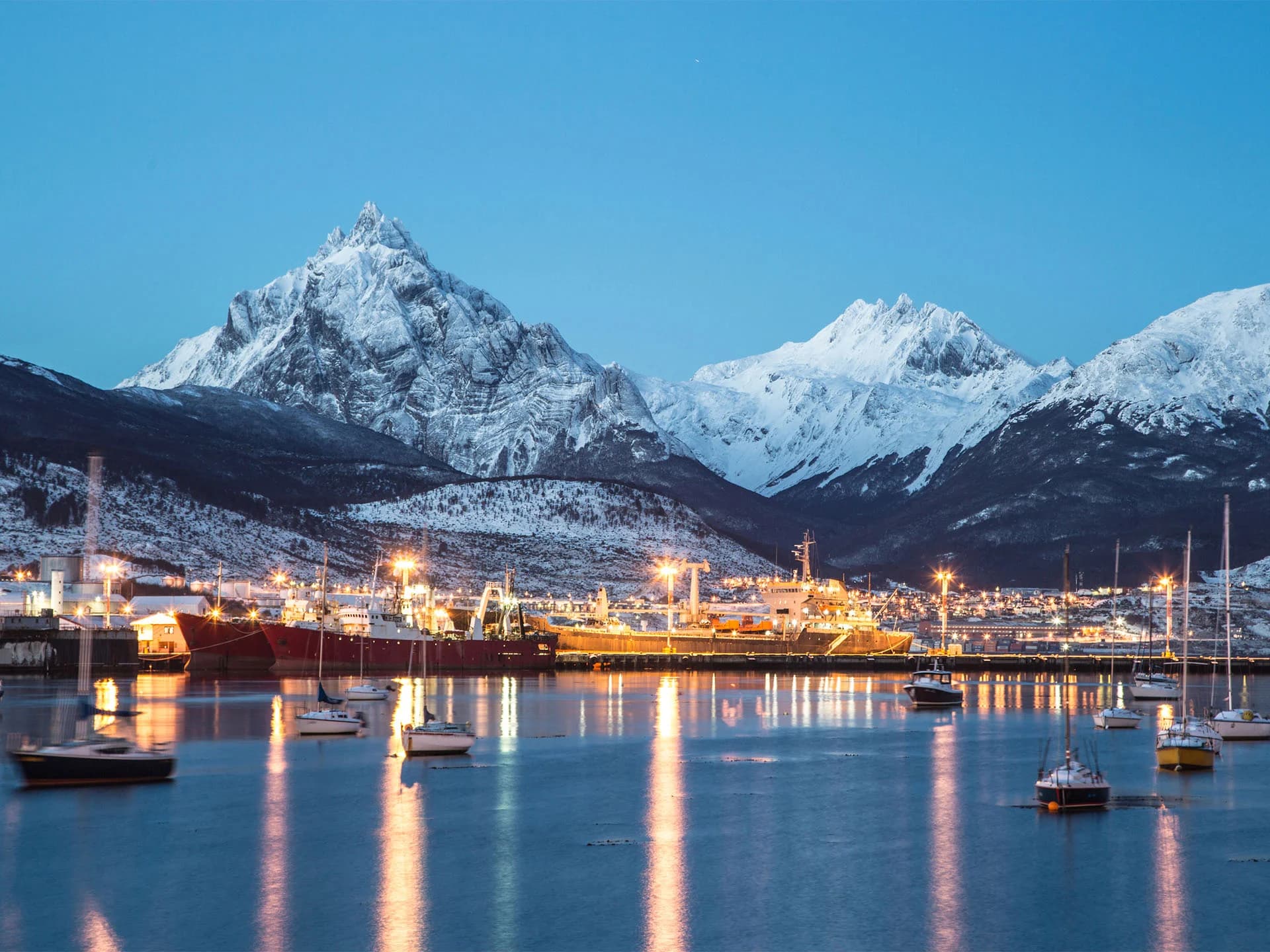 Vista panorámica de Ushuaia con montañas nevadas y el Canal Beagle al atardecer